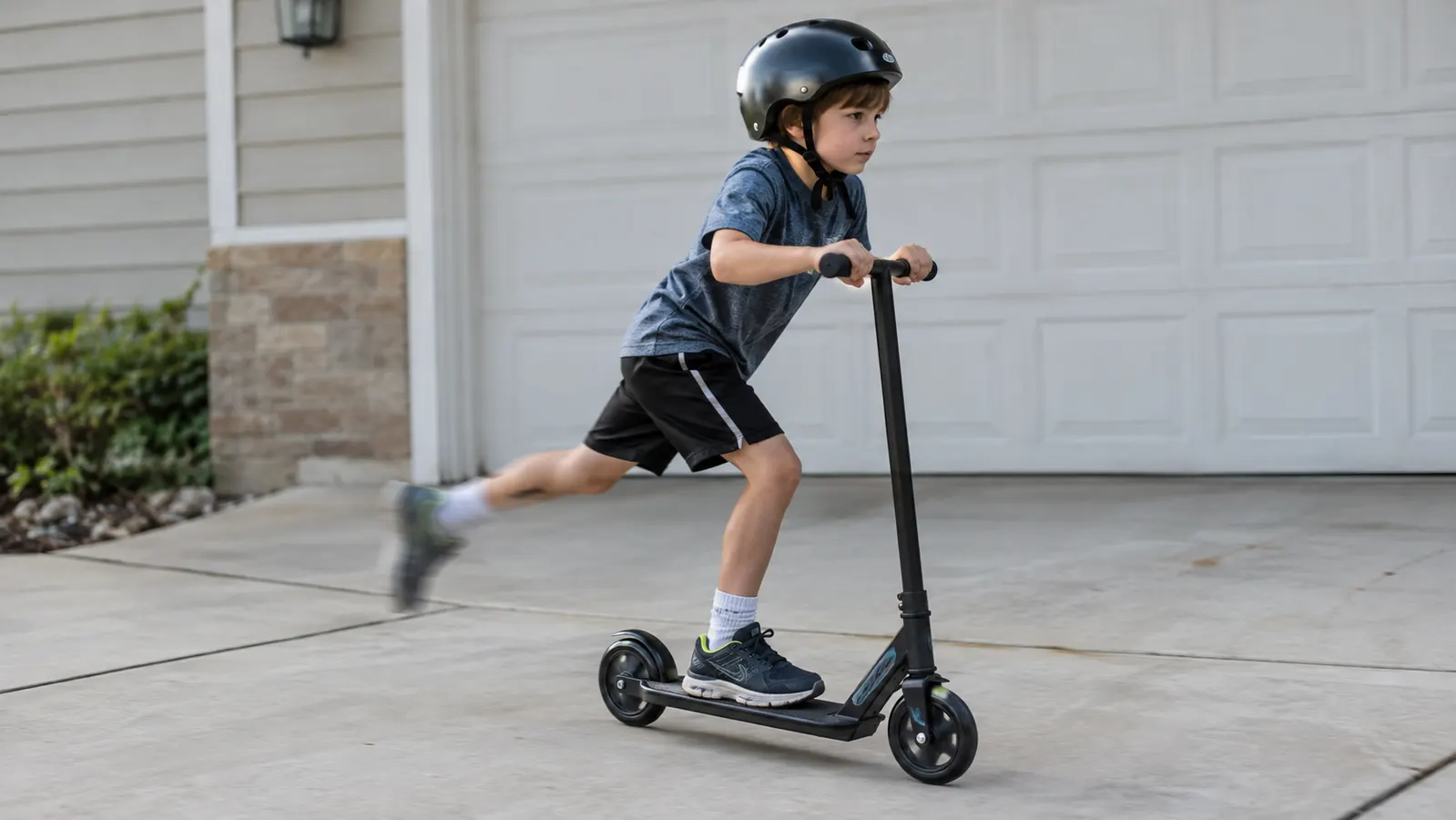 A child in a helmet practicing a scooter glide with one foot on the deck and one foot pushing